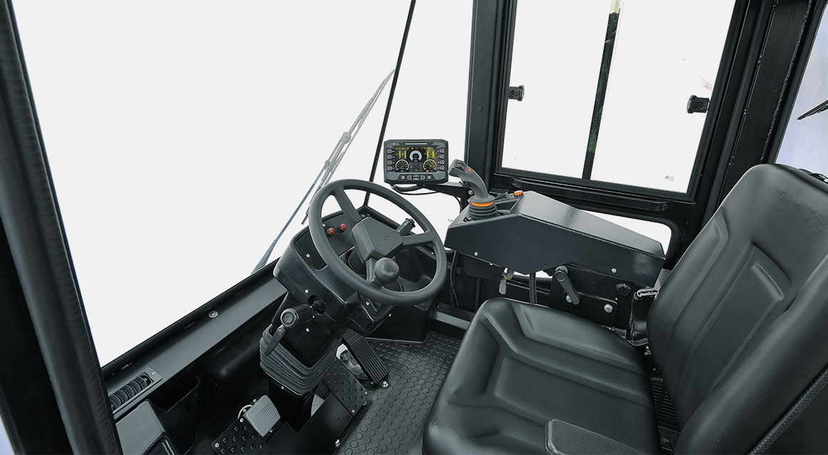 The interior of a heavy machinery operator's cab. It features a steering wheel, a digital dashboard, control levers, and a black seat.