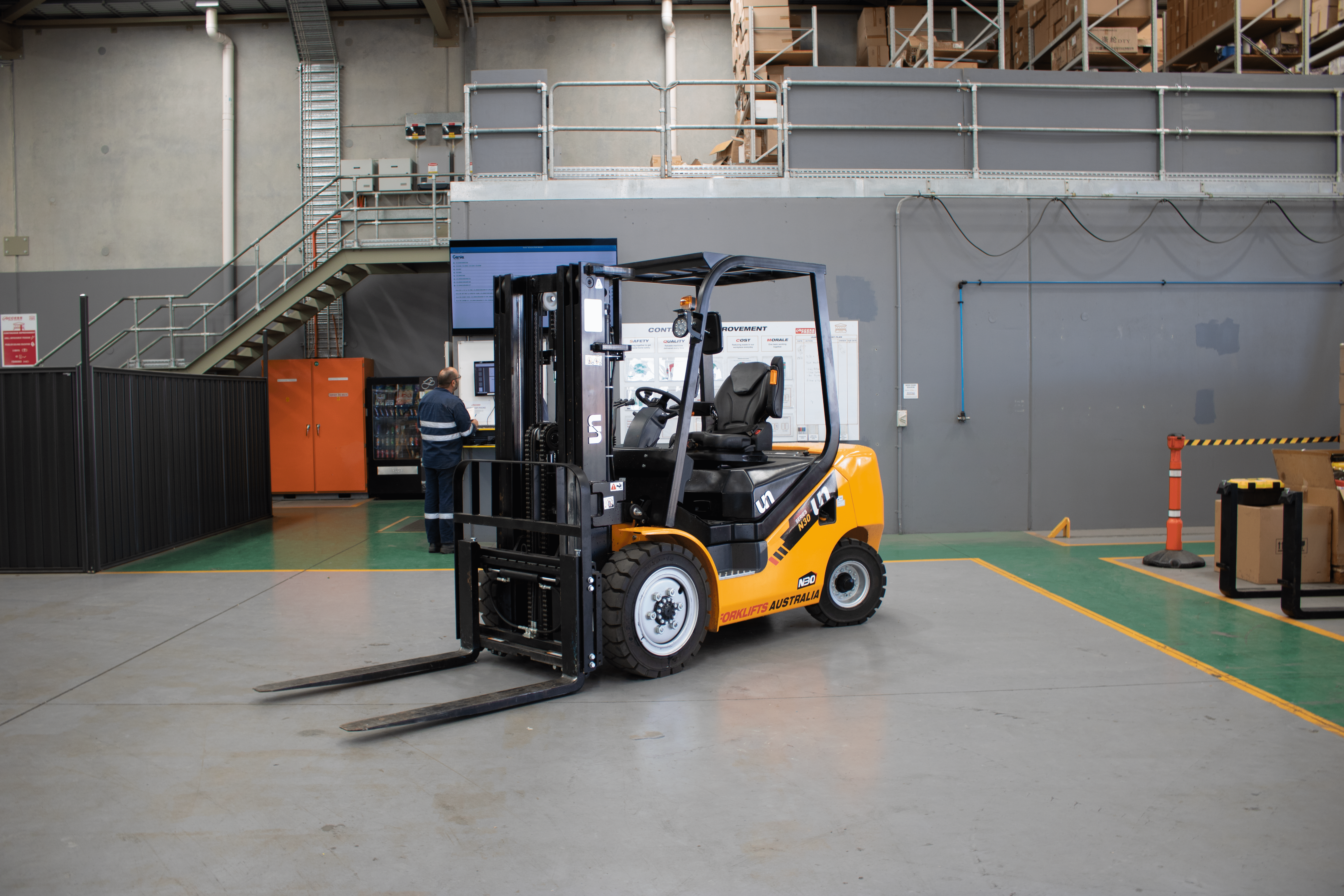 A yellow and black forklift labeled "Forklifts Australia" is parked inside a warehouse, surrounded by tall shelving. Another forklift is visible next to it. The warehouse has a high ceiling with metal beams and the floor is marked with yellow lines.